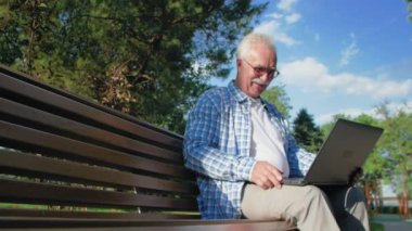 Mutlu kıdemli adam Skype 'ta konuşuyor, bahçede bankta oturuyor. Bir emekli dizüstü bilgisayarını kucağında tutuyor. Veda etmek için elini sallıyor.