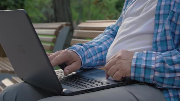 Close up of old man using computer in park. He is touching touchpad to browsing the Internet — Stock Video
