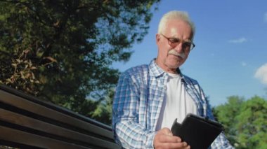 Bıyıklı yaşlı bir adam kitapta komik anlar okuyor. Yaşlı adam parkta bankta oturuyor ve kitap okuyor.