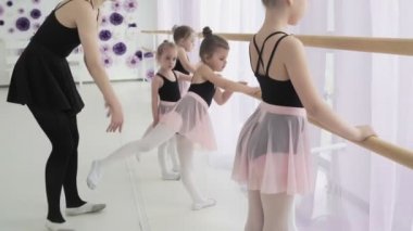 Genç balerinler son moda bale kıyafetleriyle ayak hareketleri yapıyor ve ahşap bale barı ve geniş pencereli ışıklı dans salonunda dans ediyorlar..