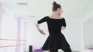 Siyah sırt çantalı profesyonel bir balerin büyük bir eğitim salonunda dans ediyor.