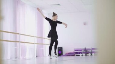 Siyah sırt çantalı profesyonel bir balerin büyük bir eğitim salonunda dans ediyor.