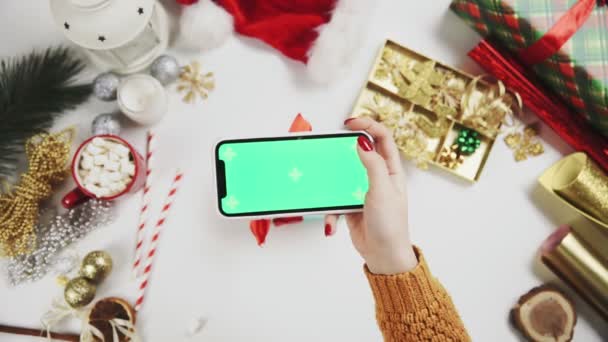 女人的手在白桌子上拍着圣诞礼物的照片。绿色屏幕电话显示屏. — 图库视频影像