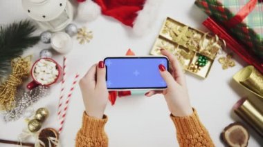 Kadın eli beyaz masada Noel hediyesinin fotoğrafını çekiyor. Krom anahtar telefon görüntüsü.