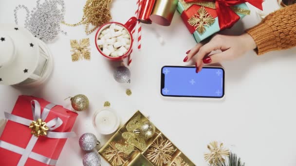 Mujer usando el teléfono inteligente con la tecla Chroma, tocando, deslizar, desplazarse hacia arriba. Decoración navideña sobre fondo de mesa blanco. Vídeo de orientación vertical de la pantalla 9: 16 — Vídeos de Stock