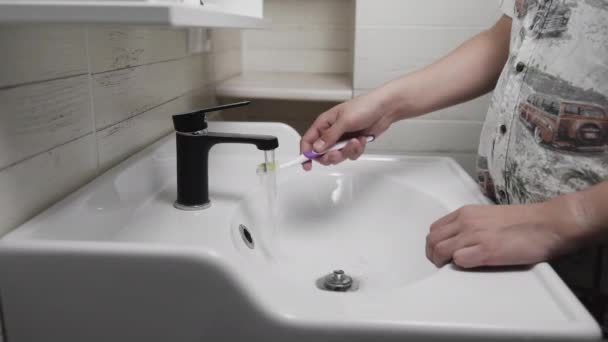 Jovem escovar os dentes com uma escova de dentes no banheiro. Close-up de mãos espremendo massa na escova — Vídeo de Stock