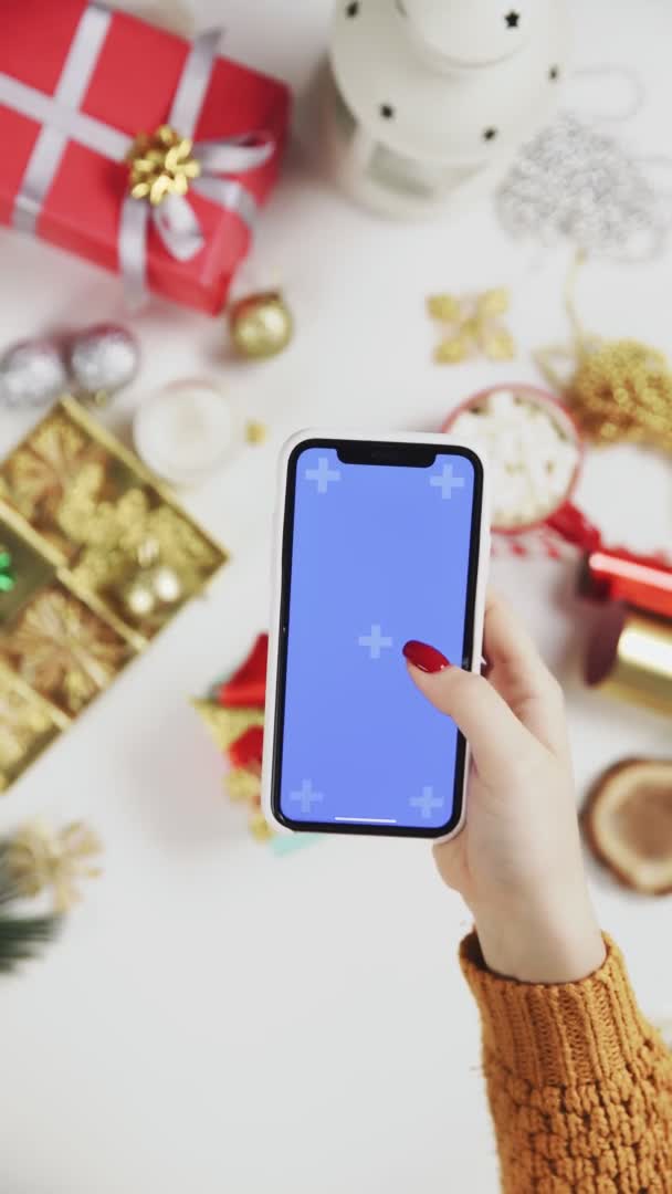 Woman using smartphone with Chroma key, tapping, swipe, scrolling up. Christmas holiday decoration on white table background. Vertical Screen Orientation Video 9:16 — Stock Video