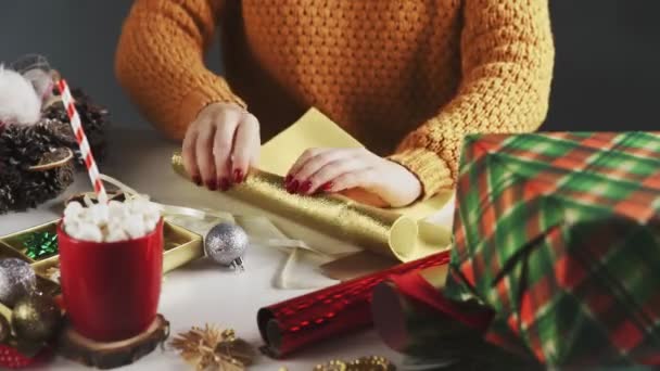 Frau bereitet goldenes Papier zum Einwickeln von Weihnachtsgeschenken auf dem Tisch mit Weihnachtsdekoration vor. — Stockvideo