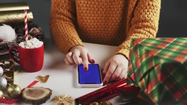 Жінка використовує смартфон за допомогою клавіші Chroma, натискання, прослуховування, прокручування вгору. Різдвяні святкові прикраси на фоні білого столу . — стокове відео
