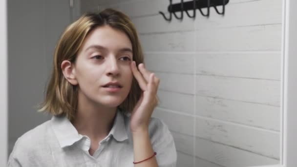 Mujer joven aplicando crema y mirando en el espejo disfrutar de la belleza natural y saludable — Vídeo de stock