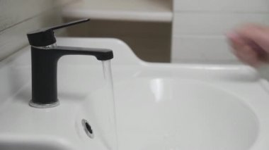 Erkek el, banyo lavabosuna su dökmek için siyah su musluğunu dönüştürüyor. Musluktan akan su.