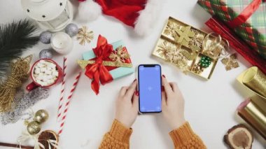 Chroma anahtarı olan akıllı telefon kullanan bir kadın, tıklatıyor, kaydırıyor, kaydırıyor. Beyaz masa arkasında Noel tatili süslemesi.