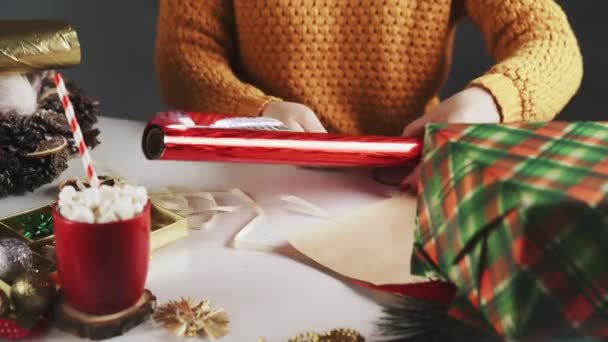 Mujer preparando papel rojo para envolver regalos de Navidad en la mesa con decoración de Navidad . — Vídeos de Stock