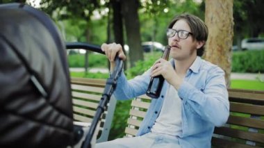 Halka açık bir yerde alkolizm. Sarhoş bir adam bira içiyor ve parkta bebek arabası sallıyor.