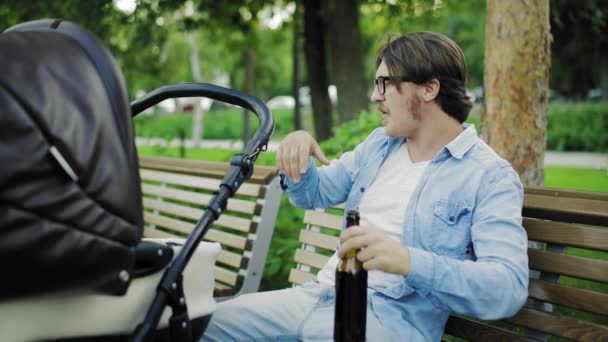 Портрет привлекательного мужчины пьет пиво, когда отдыхает со своим новорожденным ребенком — стоковое видео