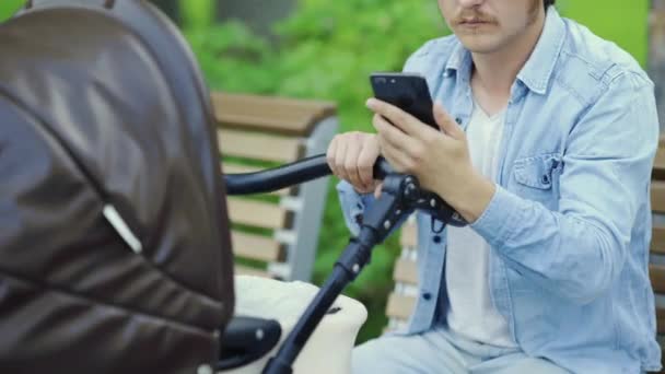 Close up of Father is using phone and swinging crying baby stroller — Stock Video