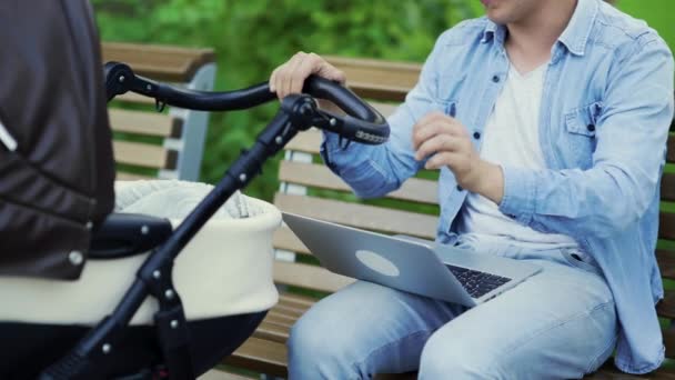 Detailní záběr Moderní mladý táta pracuje notebook a houpání baby kočárek, multitasking životní styl — Stock video