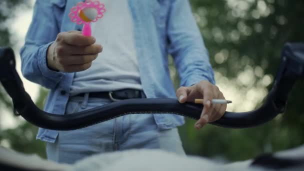 Father holding cigarette, baby stroller and playing with rattle toy, child POV — Stock Video