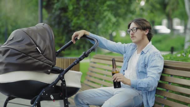 Oldalnézet vonzó férfi iszik egy sört, miközben pihen az újszülött baba — Stock videók