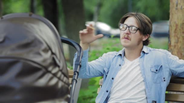 Genç adam parkta bebek arabası sallarken sigara içiyor ve bira içiyor. — Stok video