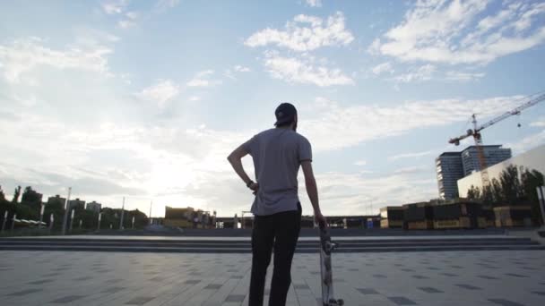 Вид сзади скейтбордиста, стоящего со скейтбордом в парке — стоковое видео