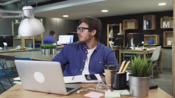 Portrait of young successful businessman sitting in modern office and loooking at the camera — Stock Video