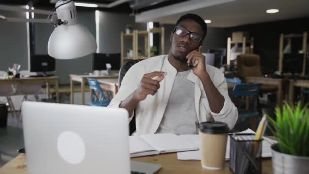Afrykanin rozmawia przez telefon komórkowy i bawi się ołówkiem w nowoczesnym biurze — Wideo stockowe