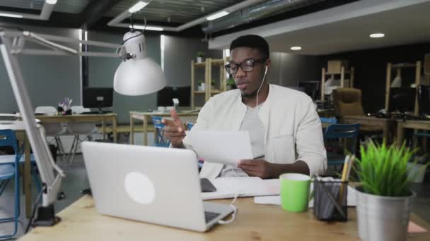 Afrikansk man med hörlurar har en videokonferens konversation i moderna kontor — Stockvideo