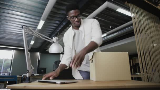 Afrikaner, der vor kurzem bei einem Unternehmen eingestellt wurde, kommen in ein neues Büro. Mann packt seine persönlichen Sachen aus — Stockvideo