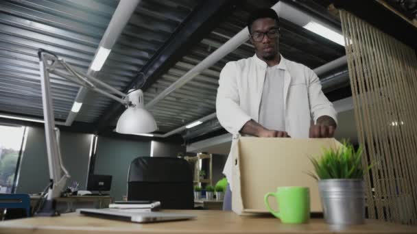 Az afrikai ember új irodába költözik. Személyes holmikat pakol a dobozba. — Stock videók