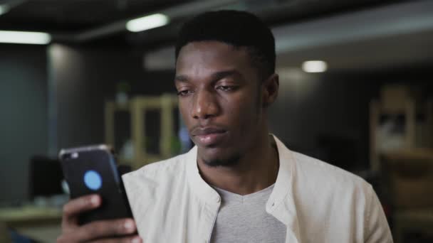 Ung afrikansk man som håller smartphone enhet sms meddelande och dricka kaffe eller te på ett modernt kontor — Stockvideo