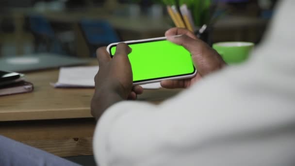 Hand of African American man scrolling web pages on horizontal Smartphone with green screen — Stock video