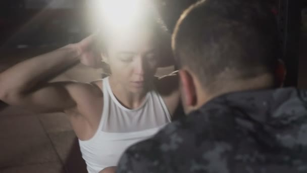 Hombre deportivo ayudando a la joven atleta a hacer sesiones en el gimnasio — Vídeos de Stock