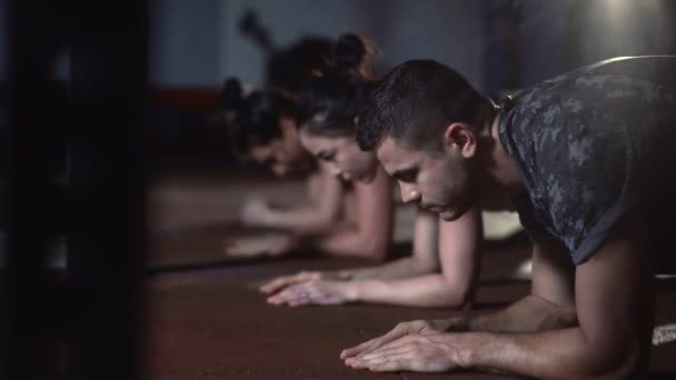 Unga sportiga attraktiva människor gör planka motion på matta på crossfit gym. — Stockvideo
