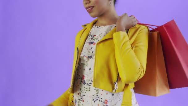 Retrato de mujer afroamericana con bolsas de compras y teléfono móvil sobre fondo púrpura en Studio. Chaqueta amarilla — Vídeos de Stock