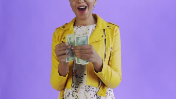 Çekici Afro-Amerikalı kadın mor bir arka plana karşı para sayıyor. Sarı ceketli. — Stok video