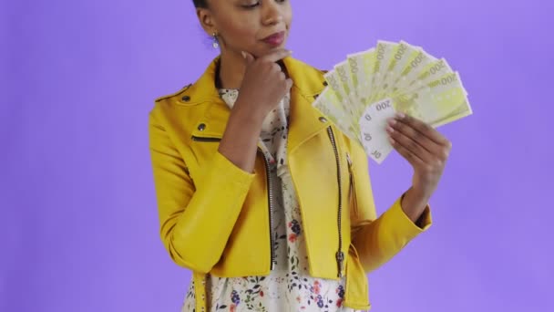 Στοχαστική επιτυχημένη αφροαμερικανή γυναίκα με χρήματα ανεμιστήρα σε μωβ φόντο στο στούντιο. Κίτρινο σακάκι — Αρχείο Βίντεο