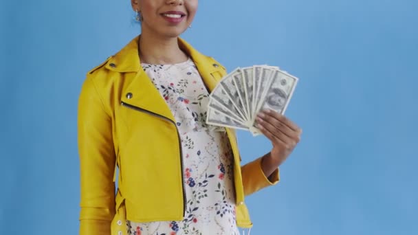Afrikai amerikai nő portréja, pénz rajongóval, kék háttér a stúdióban. Sárga kabát — Stock videók