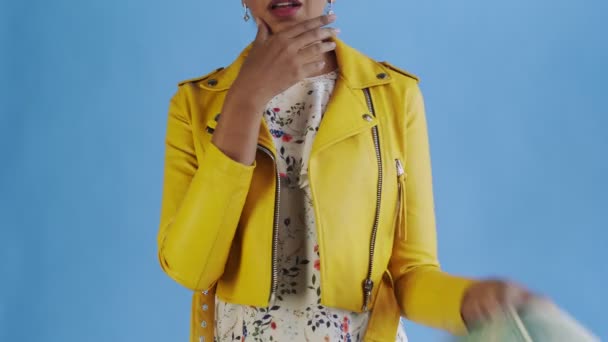 Στοχαστική επιτυχημένη αφροαμερικανή γυναίκα με χρήματα ανεμιστήρα στο μπλε φόντο στο στούντιο. Κίτρινο σακάκι — Αρχείο Βίντεο