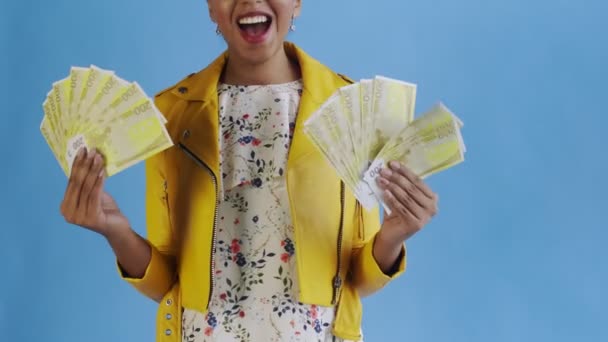 Satisfied happy excited african american woman showing money and saying O MY GOD on blue background Yellow jacket — стокове відео