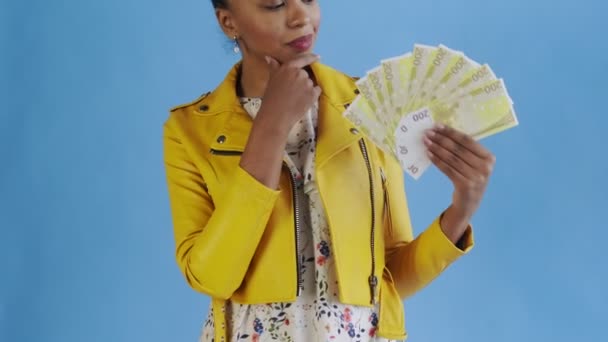 Thoughtful successful african american woman with money fan on blue Background in Studio. Yellow jacket — стокове відео