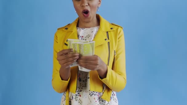 Attractive Afro american woman is counting money against a blue background Yellow jacket — Stock Video