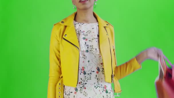 Portret van Afro-Amerikaanse vrouw met boodschappentassen en Gold credit card op groene achtergrond in Studio. Gele jas — Stockvideo