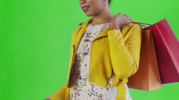 Retrato de mujer afroamericana con bolsas de compras y teléfono móvil sobre fondo verde en Studio. Chaqueta amarilla — Vídeos de Stock