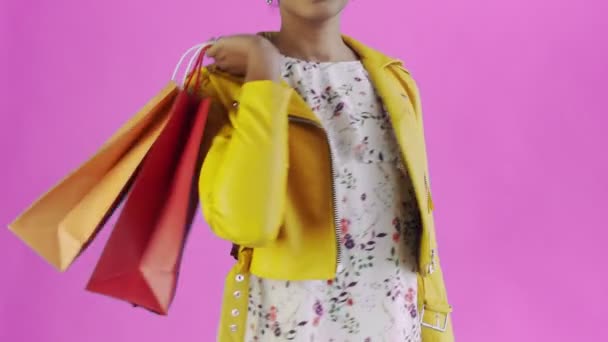 Retrato de mujer afroamericana con bolsas de compras y abanico de dinero en rosa Fondo en Studio. Chaqueta amarilla — Vídeos de Stock