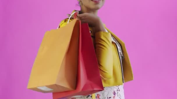 Retrato de mujer afroamericana con bolsas de compras y abanico de dinero en rosa Fondo en Studio. Chaqueta amarilla — Vídeos de Stock