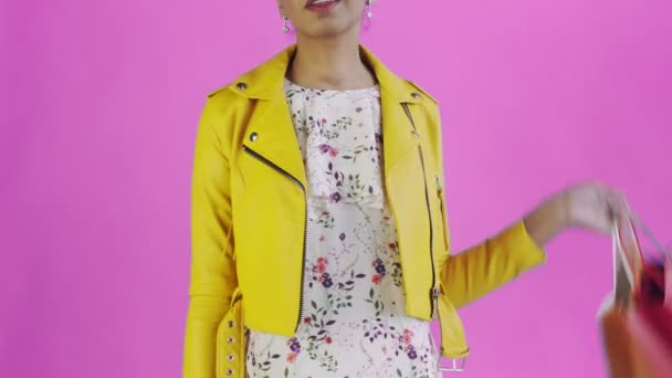 Portrait of african american woman with shopping bags and GOLD credit card on pink Background in Studio. Yellow jacket — Stock Video