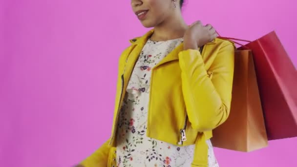 Retrato de mujer afroamericana con bolsas de compras y teléfono móvil sobre fondo rosa en Studio. Chaqueta amarilla — Vídeos de Stock