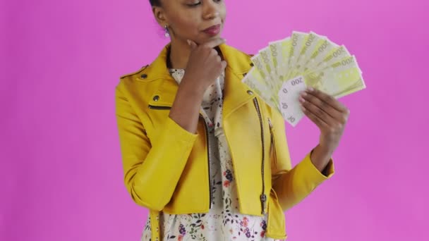 Átgondolt sikeres afro-amerikai nő pénz rajongó rózsaszín háttér stúdióban. Sárga kabát — Stock videók