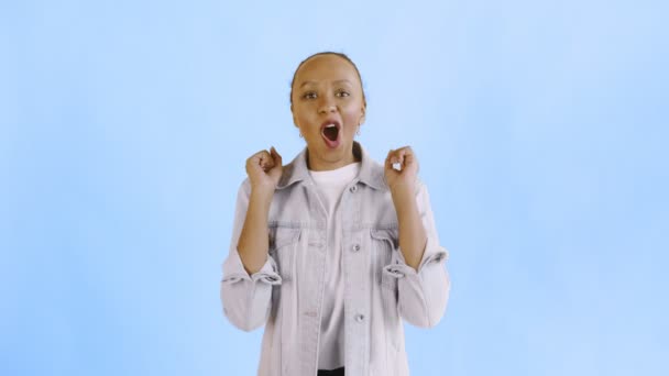 Hermosa mujer joven africana feliz diciendo OH MI DIOS y bailando sobre fondo azul chaqueta Jean — Vídeos de Stock